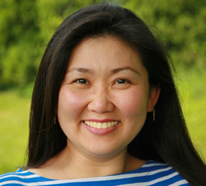 photograph of Francisca Miller smiling and standing in front of a green field and bushes