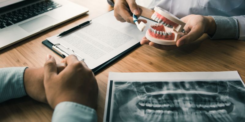 dentist showing a patient a model of teeth with an xray of teeth on the table